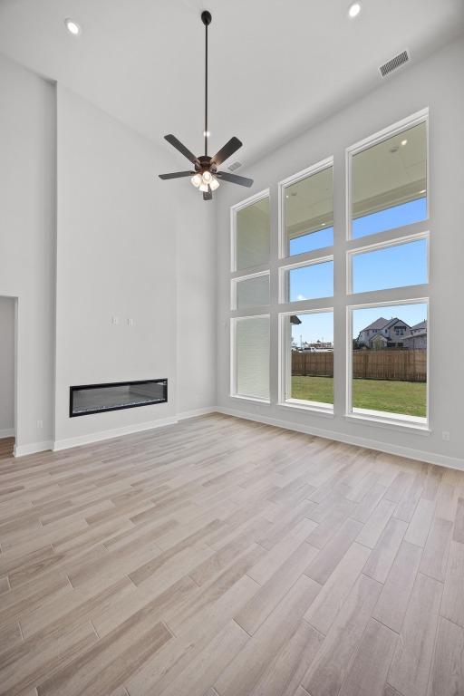 unfurnished living room featuring light wood-style floors, a ceiling fan, a glass covered fireplace, visible vents, and baseboards