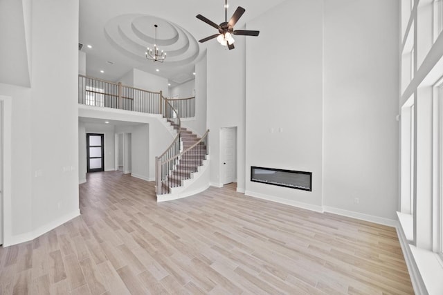unfurnished living room featuring recessed lighting, wood finished floors, a towering ceiling, and stairs