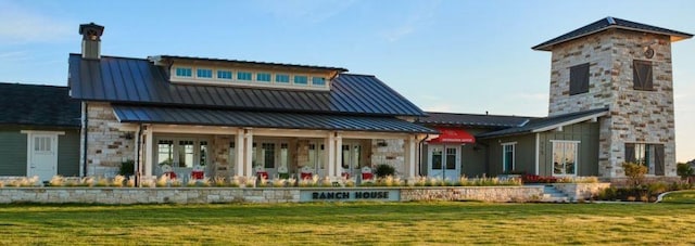 rear view of house with a standing seam roof, a lawn, metal roof, stone siding, and a chimney