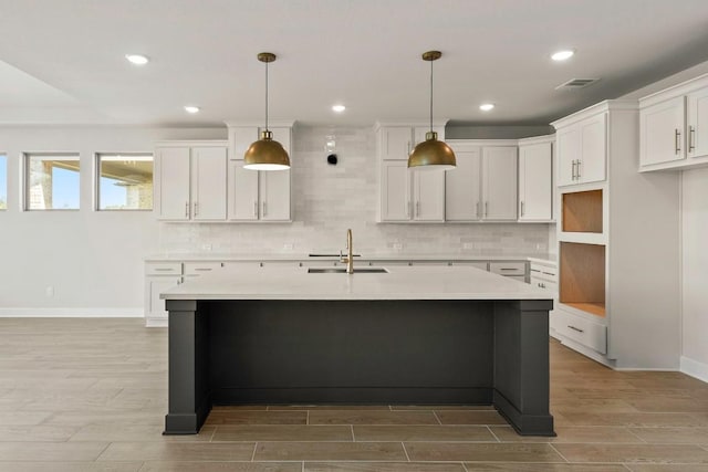 212 Ranchland Pass, Liberty Hill, TX 78642 - kitchen featuring a sink, wood finish floors, a center island with sink, backsplash, and white cabinetry