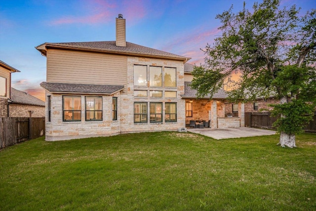 back of property at dusk with a fenced backyard, a chimney, a patio area, and stone siding