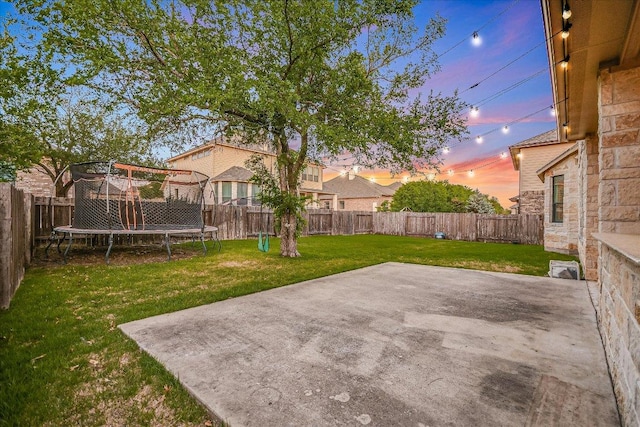 yard at dusk with a patio, a fenced backyard, and a trampoline