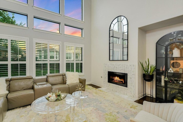 living room with a tiled fireplace, baseboards, wood finished floors, and a towering ceiling