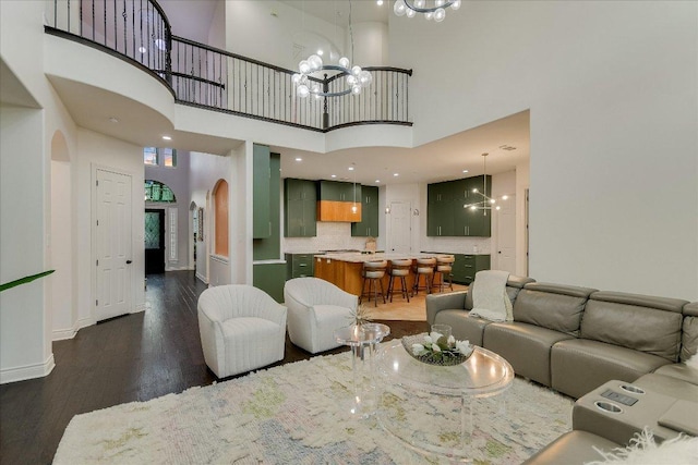living room with arched walkways, a towering ceiling, wood finished floors, and a notable chandelier