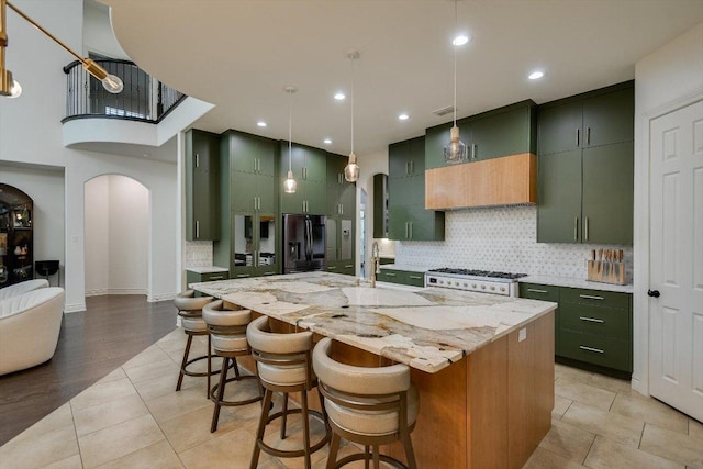 kitchen with backsplash, arched walkways, black fridge, and green cabinets
