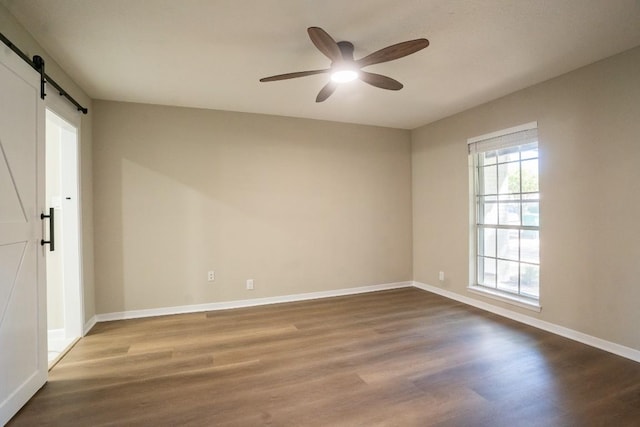 empty room with a barn door, ceiling fan, baseboards, and wood finished floors