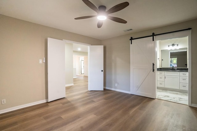 unfurnished bedroom with visible vents, baseboards, a barn door, a sink, and wood finished floors