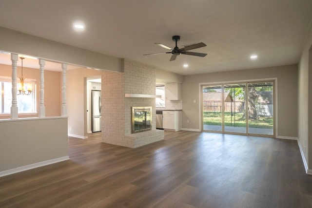 unfurnished living room with recessed lighting, dark wood-style flooring, ceiling fan with notable chandelier, and a brick fireplace