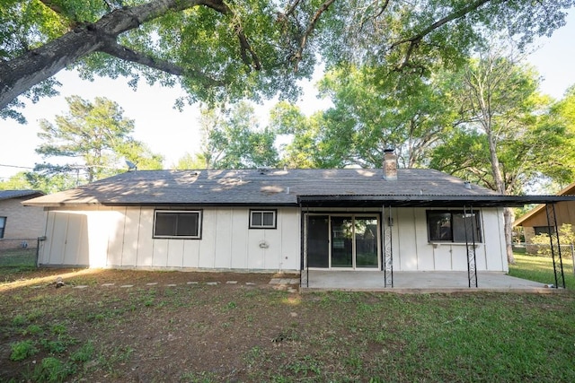 rear view of house with a patio area, board and batten siding, a chimney, and a lawn