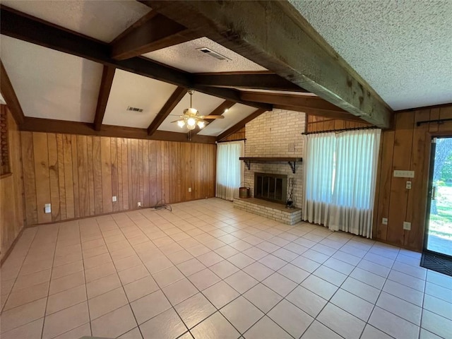604 E Kerr St, Burnet, TX 78611 - unfurnished living room with wood walls, a ceiling fan, light tile patterned floors, a brick fireplace, and a textured ceiling