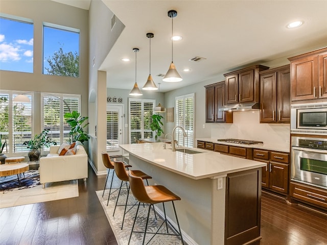 kitchen with a sink, appliances with stainless steel finishes, light countertops, dark wood finished floors, and under cabinet range hood