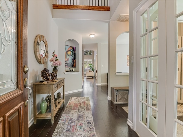 foyer featuring arched walkways, visible vents, baseboards, and dark wood finished floors