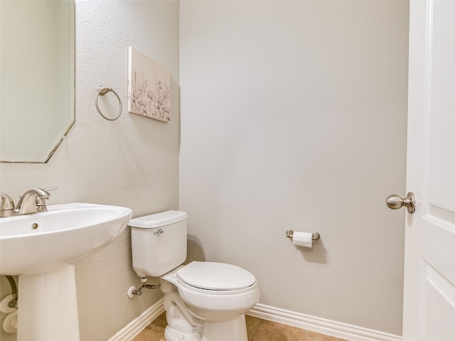 half bathroom featuring tile patterned floors, baseboards, a sink, and toilet