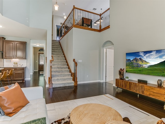 living room featuring stairway, arched walkways, dark wood-type flooring, and a high ceiling