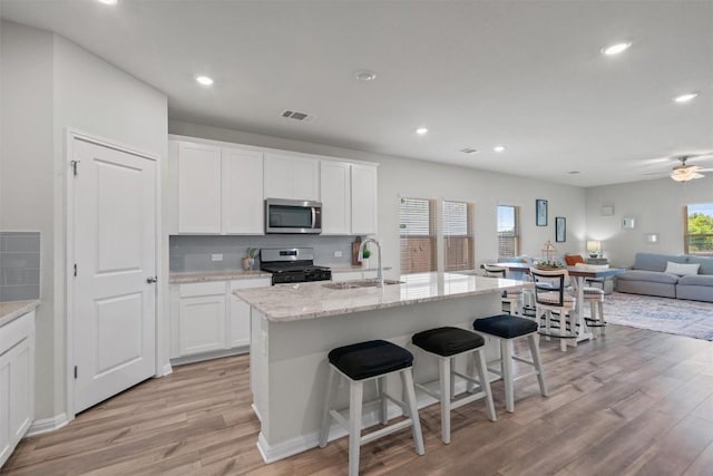 506 Windy Reed Rd, Hutto, TX 78634 - kitchen with appliances with stainless steel finishes, light wood-type flooring, open floor plan, white cabinets, and a breakfast bar