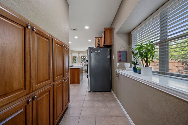 20300 Wayzata Ct, Pflugerville, TX 78660 - kitchen with freestanding refrigerator, brown cabinetry, light tile patterned floors, light countertops, and a textured wall