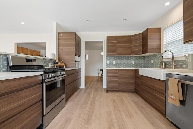 kitchen with tasteful backsplash, light countertops, stainless steel range with gas cooktop, modern cabinets, and a sink