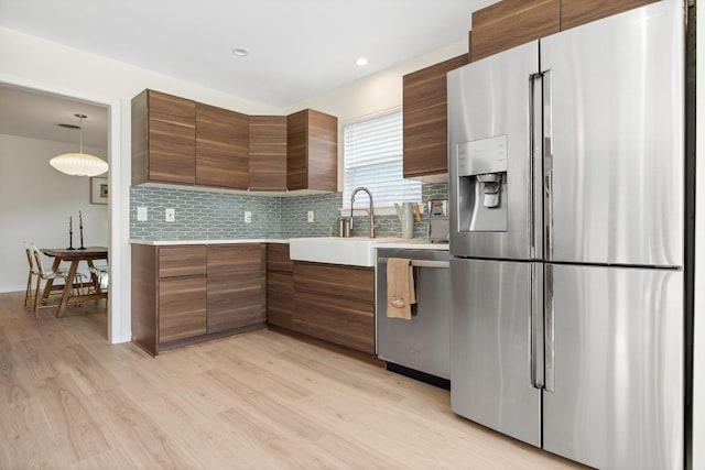 kitchen with modern cabinets, light wood-type flooring, appliances with stainless steel finishes, a sink, and light countertops