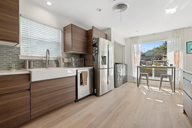 kitchen featuring washer / clothes dryer, visible vents, a sink, appliances with stainless steel finishes, and light wood-style flooring