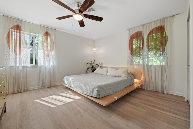 bedroom featuring multiple windows, baseboards, a ceiling fan, and wood finished floors