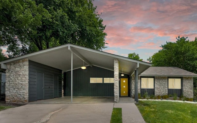 mid-century home with a lawn, driveway, stone siding, and an attached carport