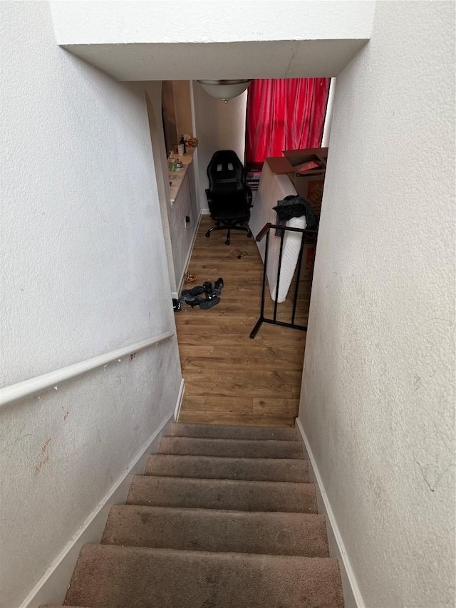 staircase featuring a textured wall, baseboards, and wood finished floors