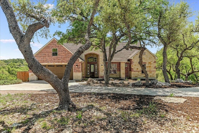 english style home with a garage, brick siding, fence, and concrete driveway