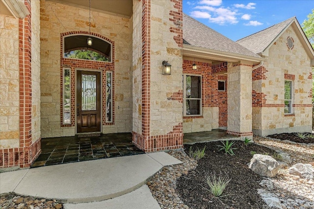 entrance to property featuring brick siding, a porch, stone siding, and roof with shingles