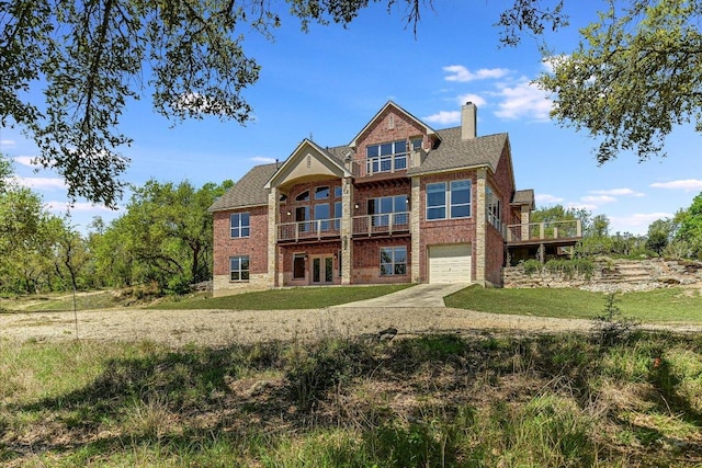 back of property with a chimney, driveway, an attached garage, brick siding, and a lawn