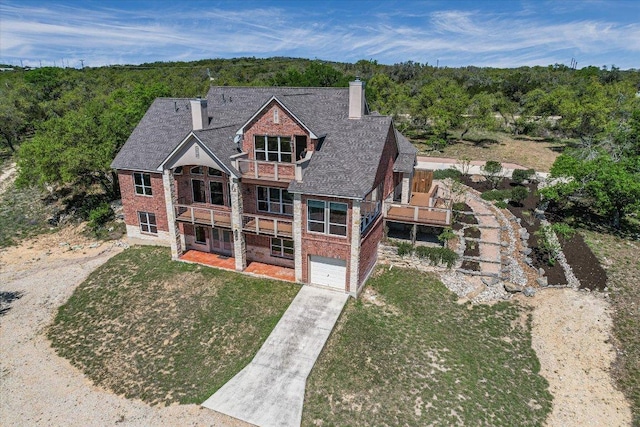 view of front of home featuring concrete driveway, a balcony, a chimney, brick siding, and a garage