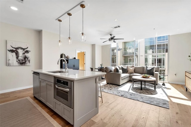 kitchen with a sink, light countertops, appliances with stainless steel finishes, gray cabinetry, and light wood-style flooring