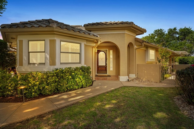 30203 Hacienda Ln, Georgetown, TX 78628 - view of exterior entry with a tile roof, stucco siding, a yard, and a gate