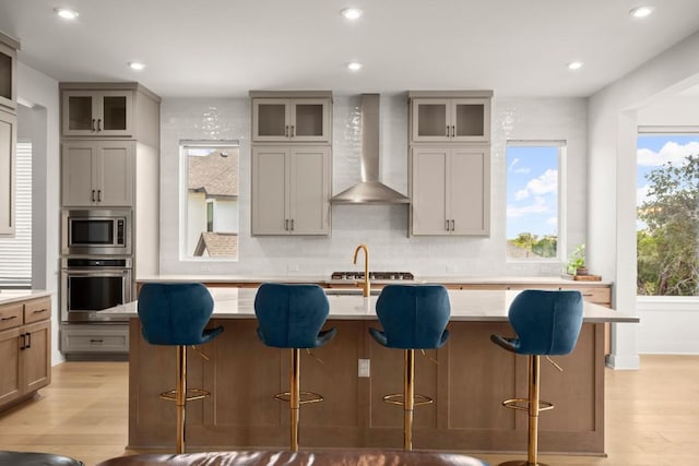 6701 Adventures Pl, Jonestown, TX 78645 - kitchen featuring wall chimney range hood, appliances with stainless steel finishes, decorative backsplash, and light wood-style floors