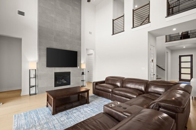 6701 Adventures Pl, Jonestown, TX 78645 - living area with wood finished floors, a tiled fireplace, visible vents, stairway, and a towering ceiling