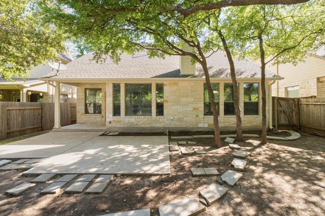 rear view of property featuring a fenced backyard, a patio area, roof with shingles, and stone siding