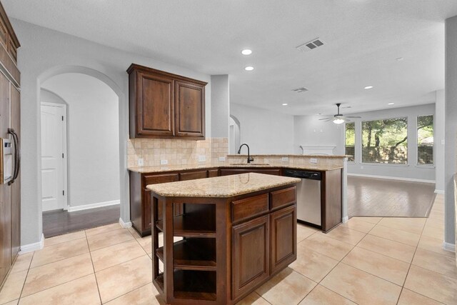 kitchen featuring a sink, arched walkways, stainless steel dishwasher, and a peninsula