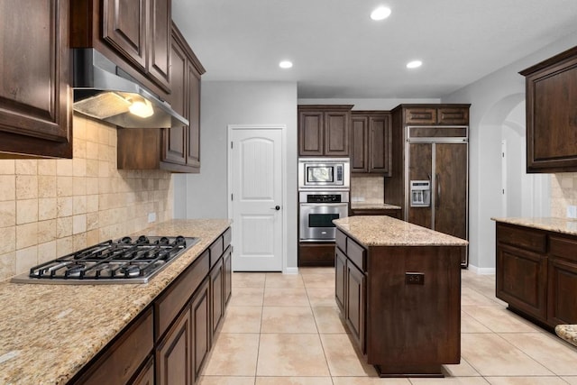 4014 Remington Rd, Cedar Park, TX 78613 - kitchen featuring built in appliances, exhaust hood, dark brown cabinetry, tasteful backsplash, and arched walkways