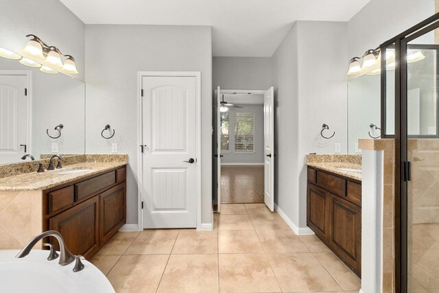 full bath featuring a sink, tile patterned flooring, baseboards, a shower stall, and two vanities