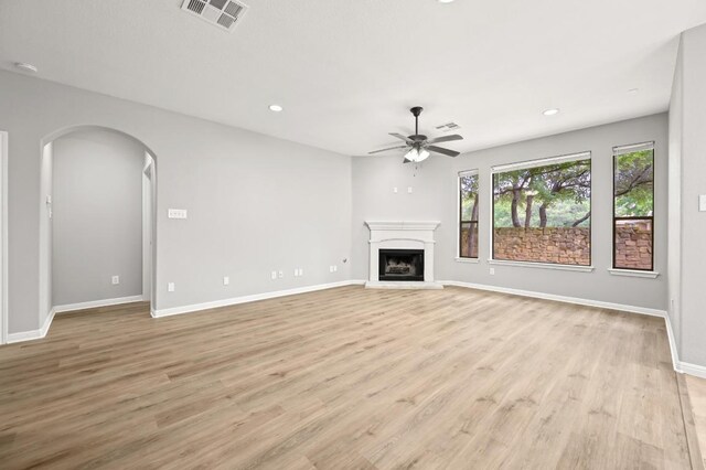 unfurnished living room with a ceiling fan, arched walkways, visible vents, and light wood-type flooring