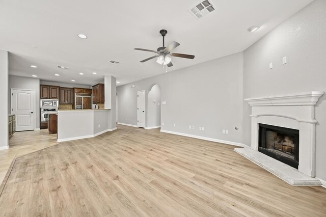 unfurnished living room with a ceiling fan, visible vents, baseboards, a fireplace with raised hearth, and recessed lighting