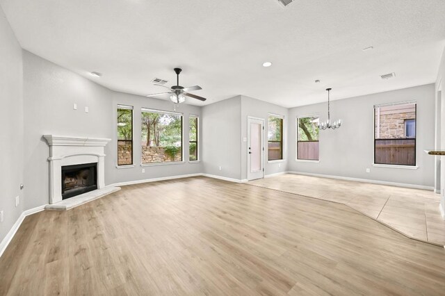 unfurnished living room with visible vents, light wood-type flooring, baseboards, a fireplace with raised hearth, and ceiling fan with notable chandelier