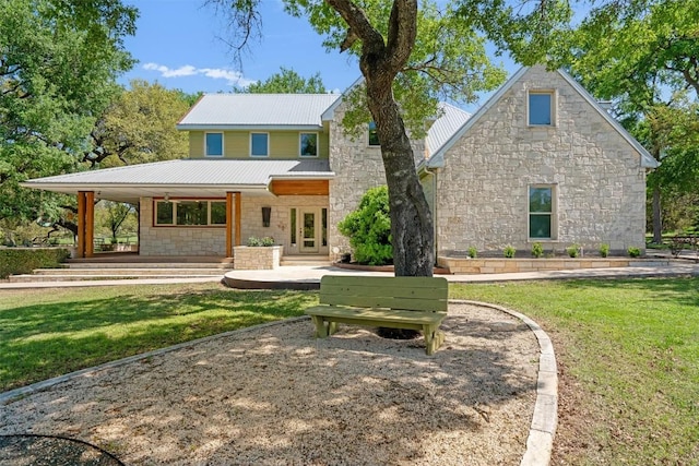 back of house featuring stone siding, a lawn, and metal roof