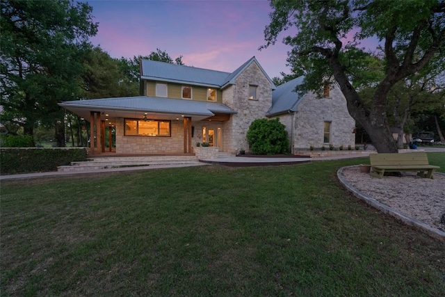 back of house at dusk with stone siding, a lawn, a porch, and metal roof