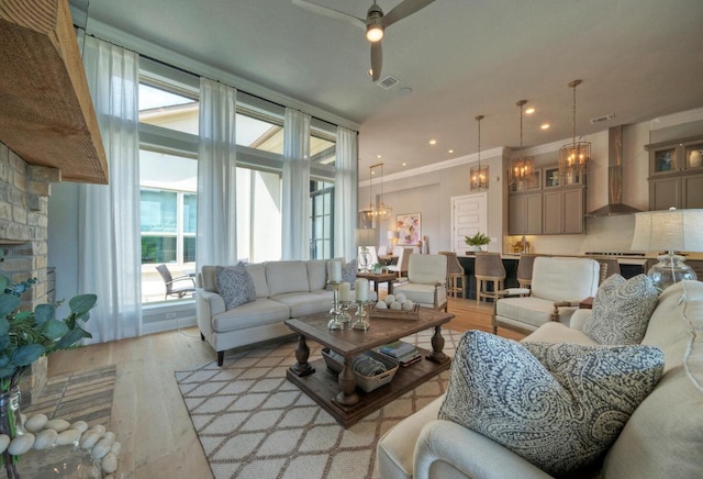 living room featuring visible vents, light wood-style flooring, and ceiling fan with notable chandelier