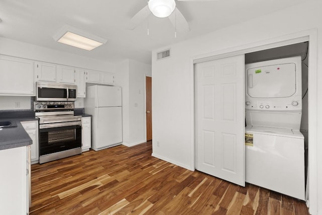 21459 Coyote Trl Unit B4, Lago Vista, TX 78645 - kitchen featuring appliances with stainless steel finishes, stacked washer and clothes dryer, white cabinetry, wood finished floors, and dark countertops