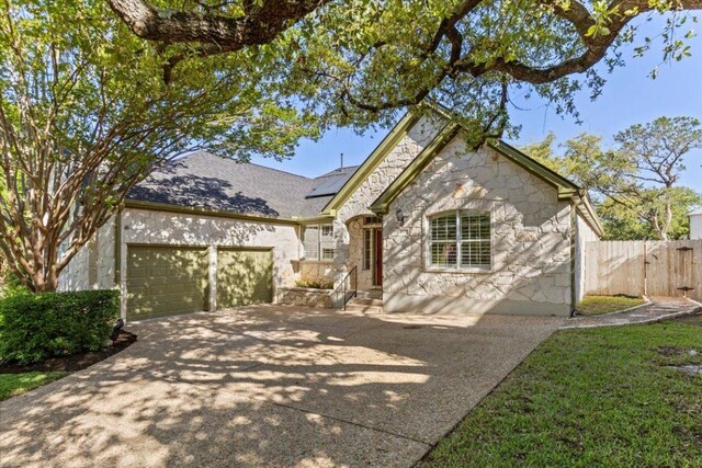 8312 Jancy Dr, Austin, TX 78750 - view of front of property featuring concrete driveway, stone siding, a garage, roof mounted solar panels, and a gate