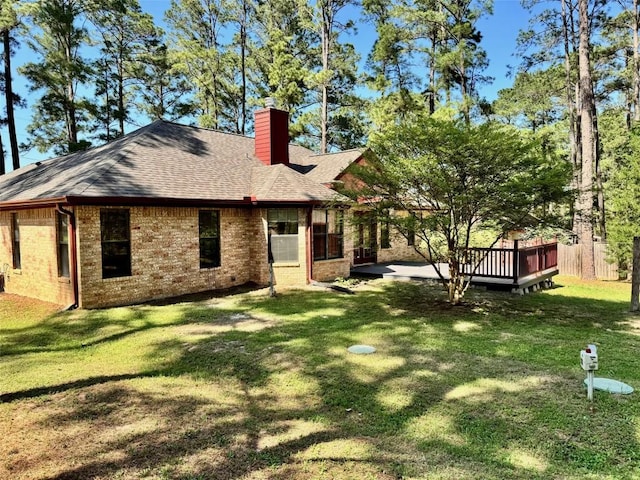 rear view of property with roof with shingles, a yard, brick siding, and a chimney