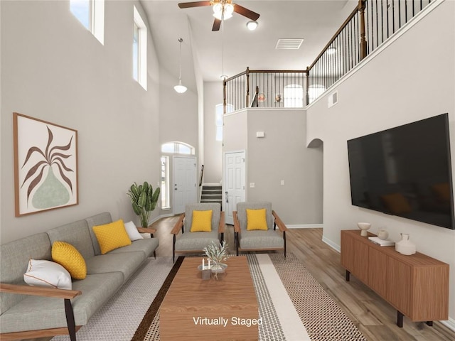 living room with a ceiling fan, baseboards, wood finished floors, a towering ceiling, and visible vents