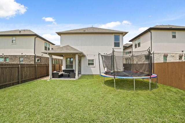 rear view of property with an outdoor living space, a trampoline, a fenced backyard, a yard, and stucco siding