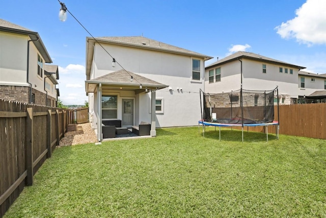 rear view of property with a fenced backyard, a trampoline, stucco siding, and a yard